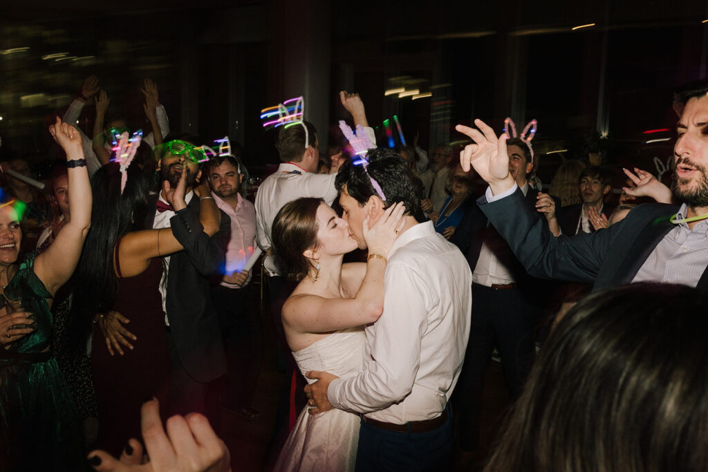 bride and groom kissing on the dance floor while guests dance around them with glow lights