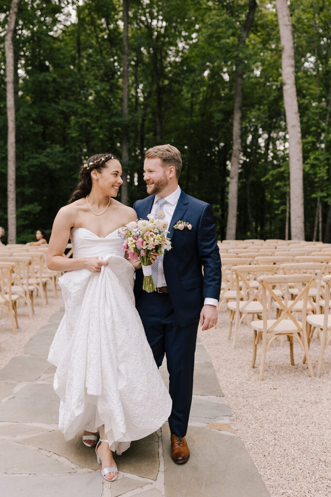 ethereal bride and groom walking down an empty aisle of bluestone pavers, surrounding by green, tall trees on a sunny day
