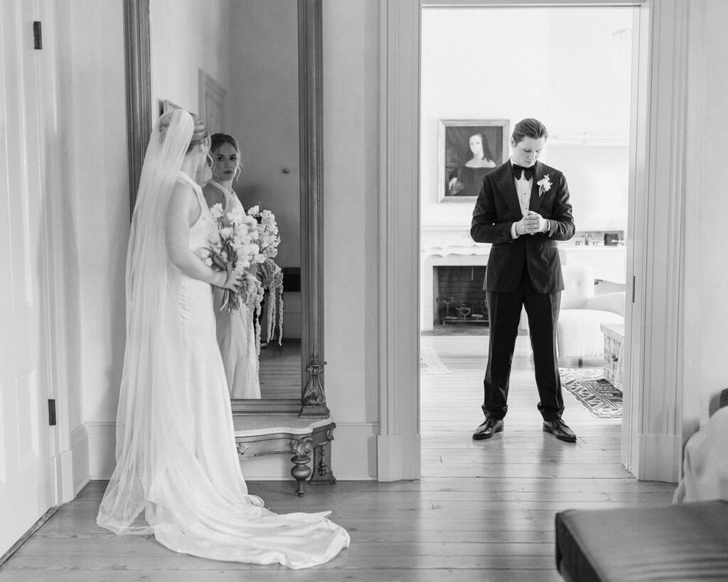 bride looking in mirror outside of room where groom waits for first look reveal