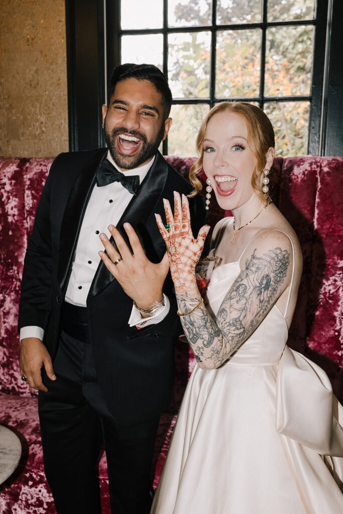 bride and groom showing off rings with open-mouth smiles